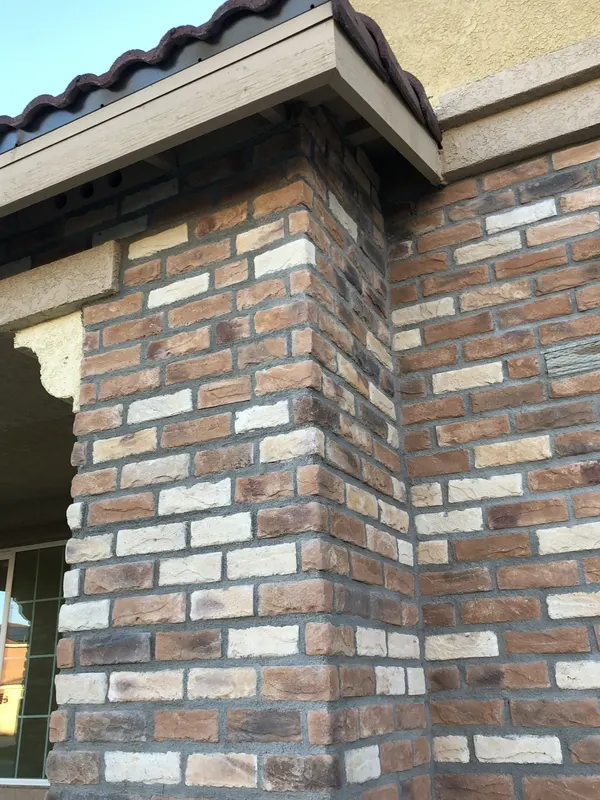 Brick veneer clads a column corner beneath a tile roof edge and stucco fascia.