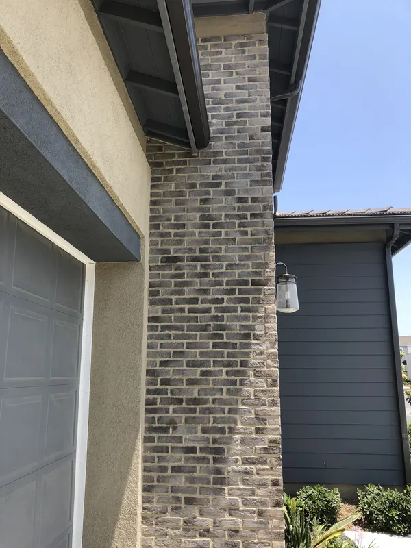 A blended grey brick veneer pier anchors the corner of a home beside a mounted lantern fixture.