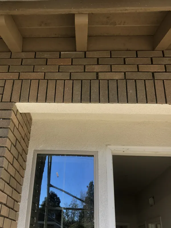 Brick veneer corner with a soldier course above a window opening, beneath an exposed wood eave.