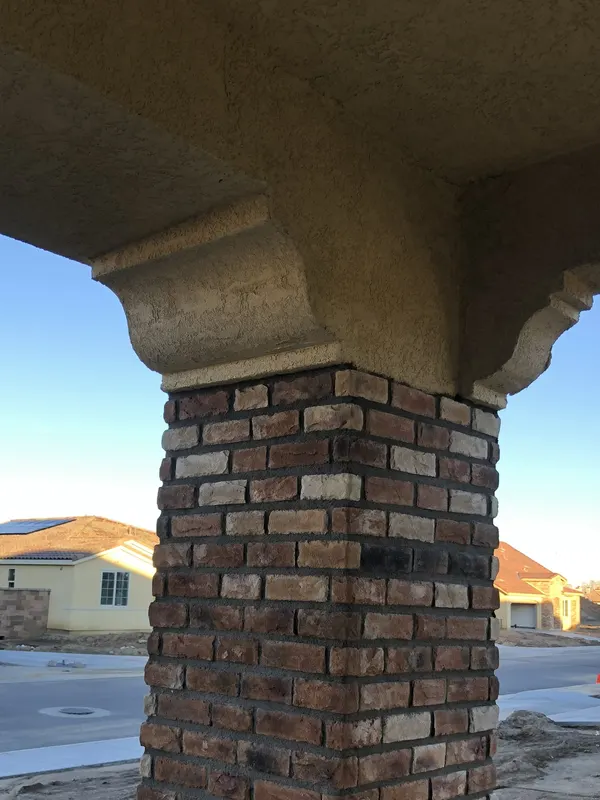 A brick veneer column supports a stuccoed roof overhang at a residential entry.