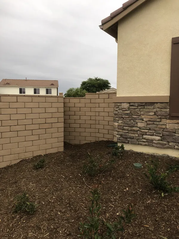 Tan split-face CMU wall divides the side yard; stone veneer wainscot at the house corner.