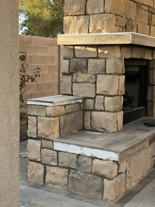Finished stacked-stone outdoor fireplace with wood mantel shelf and raised hearth seating.