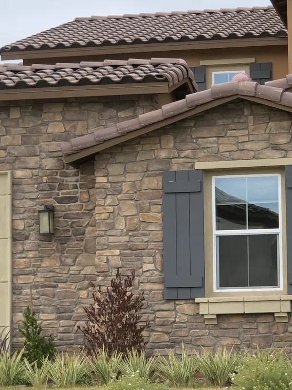 Manufactured stone veneer covers the home's exterior around a window and shutters.
