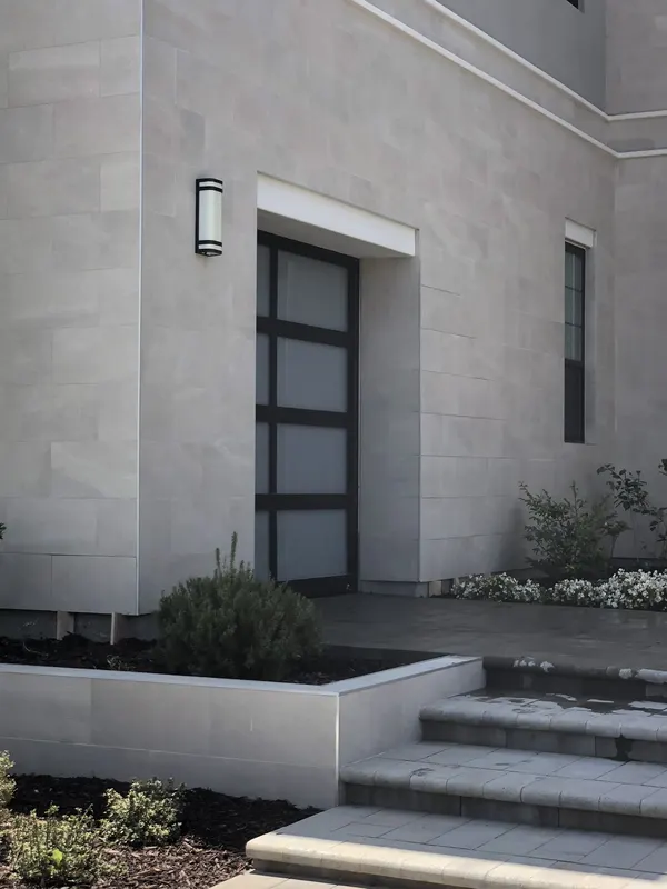 Limestone-clad entry with a dark modern door, paver steps, and finished landscaping.
