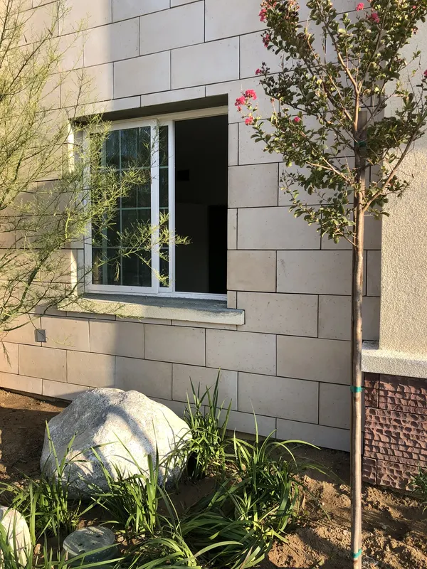 Cream limestone-look block veneer surrounding a window, laid in a running-bond pattern.