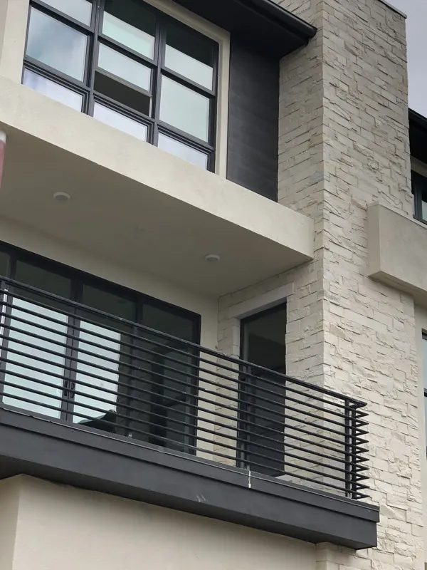Finished pale stacked stone veneer wraps an exterior corner column beside a modern black-framed balcony.