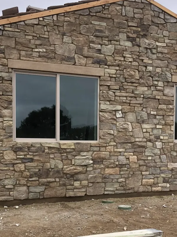Stone veneer columns and wainscot on a single-story stucco home, with the surrounding lot unfinished.