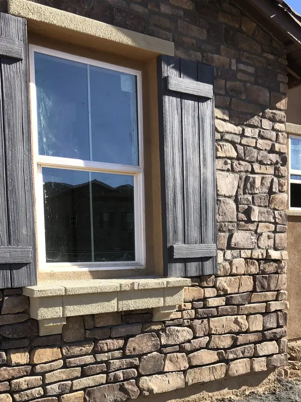 Manufactured stone veneer surrounds a window fitted with a precast sill cap.