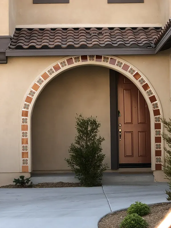 A hand-painted tile border traces a stucco archway over the front door beneath a clay tile roof.